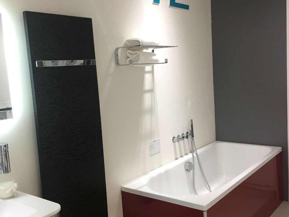 A deep double-ended bath on a burgundy panel with an LED mirror in the Elite Bathrooms showroom