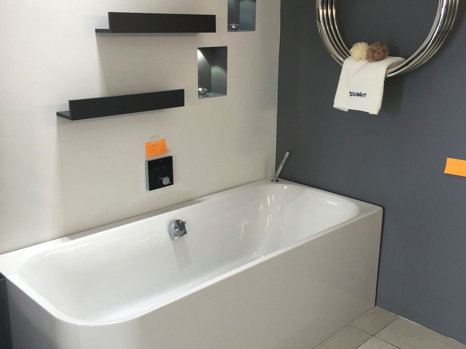 Round illuminated mirror above a stone basin with a tiled shower screen behind